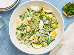 A bowl of potato salad garnished with herbs and sliced boiled eggs