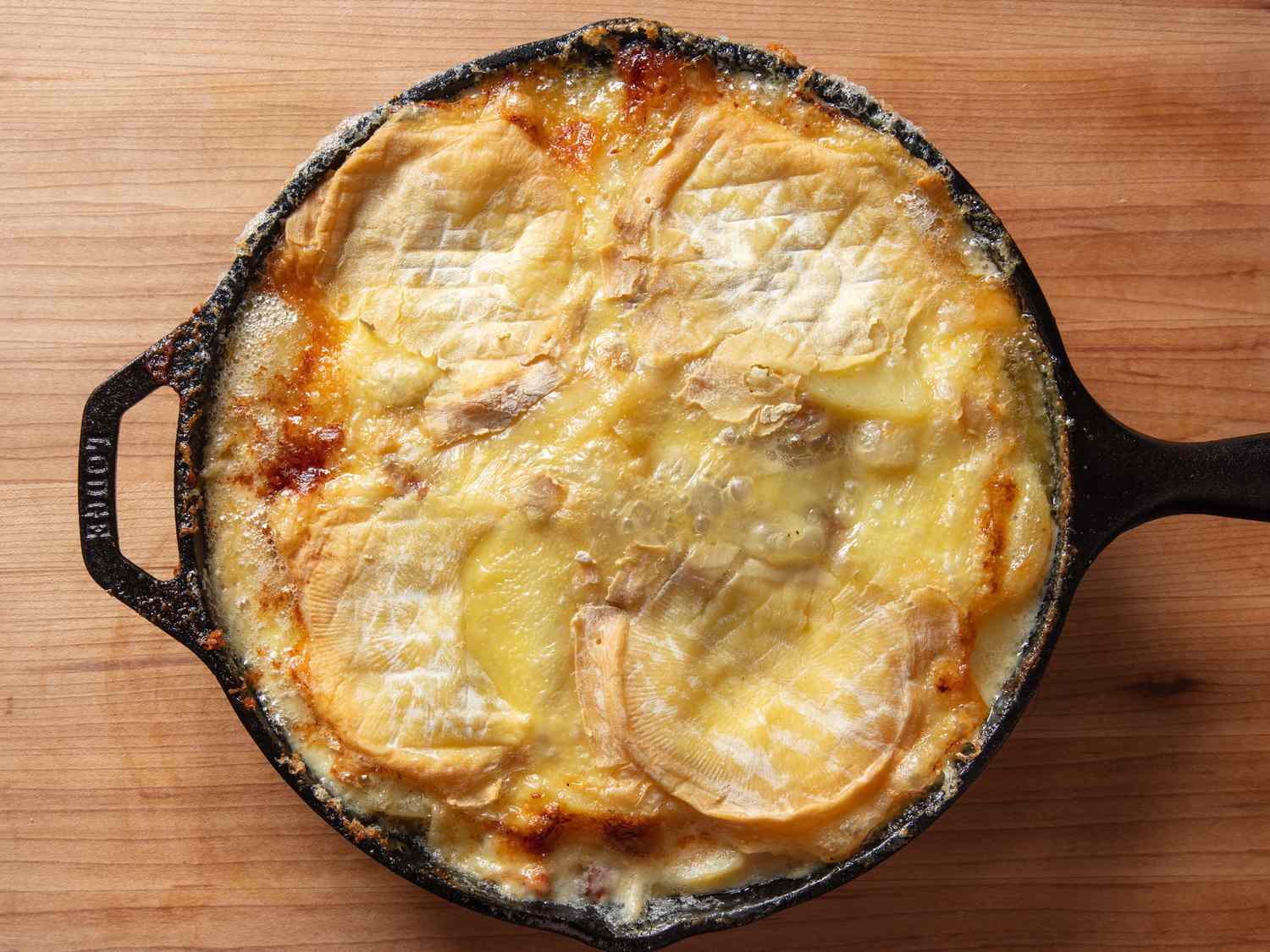 The baked tartiflette in a cast iron skillet, with the cheese melted on top.