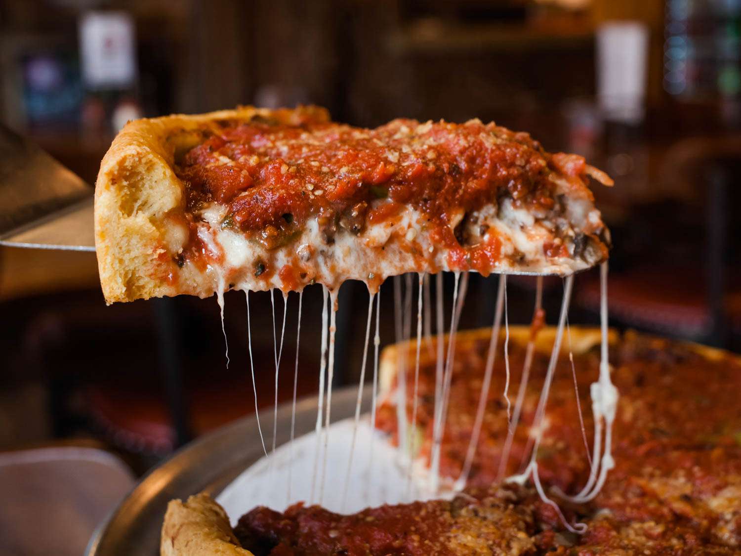 Closeup of a slice of deep dish pizza being held aloft in fron of the camera at Bartoli's.