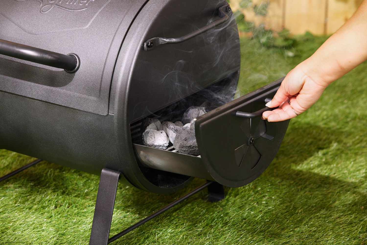 A person pulling out the firebox on the Char-Griller grill.