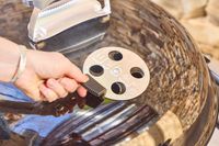 A hand touching the top of the Weber Performer Deluxe Charcoal Grill 22