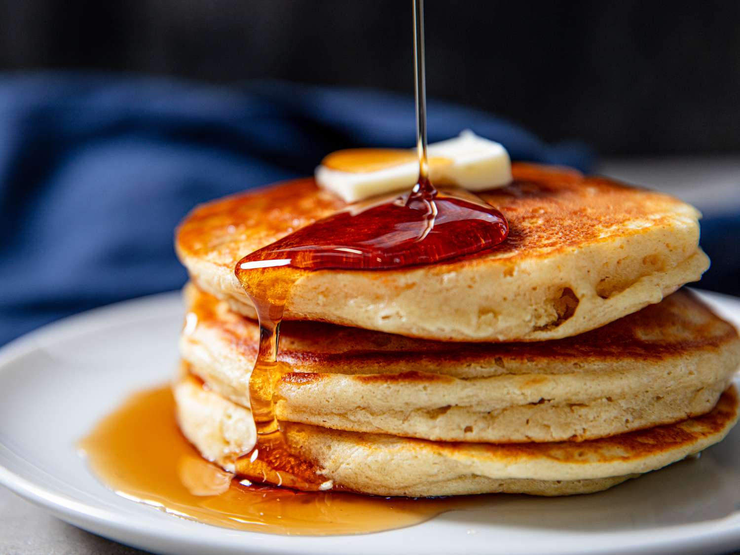 A stack of pancakes topped with butter and syrup being poured over them