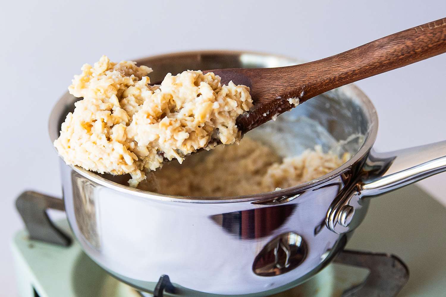 A wooden spoon holding oatmeal above a stainless steel pot