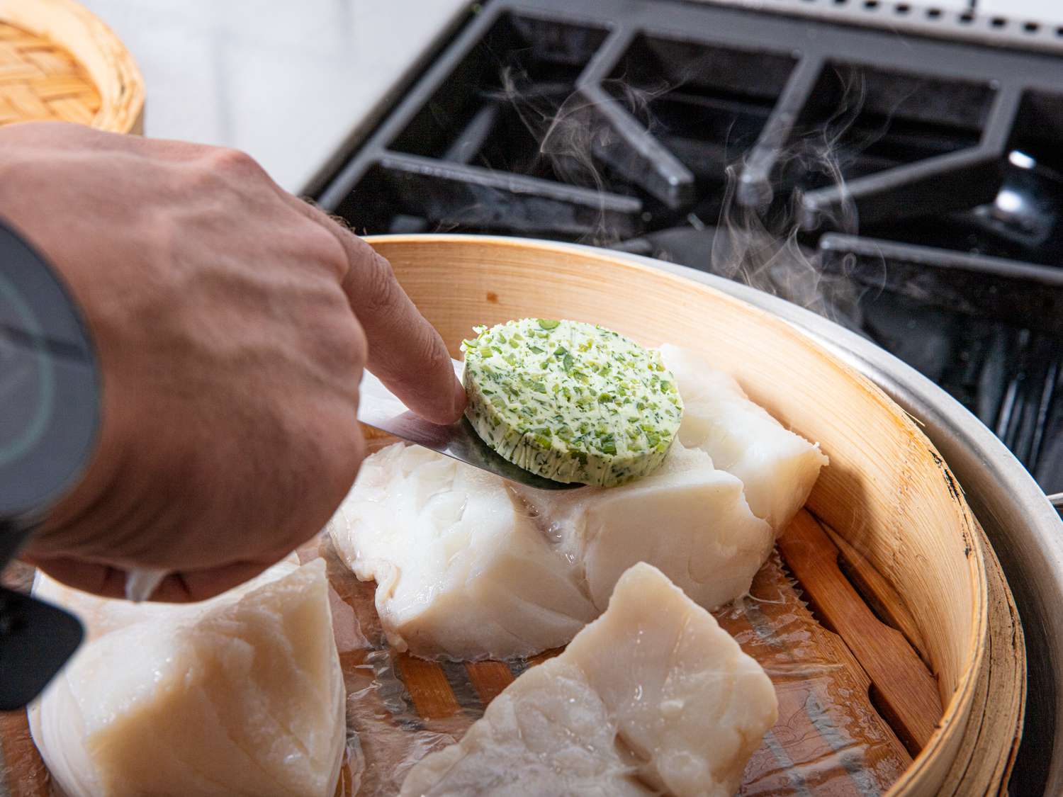 A hand placing a thick, round slice of compound butter on a steamed fish fillet.