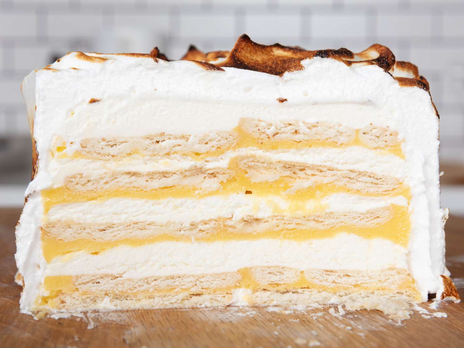 Side view of layers inside a slice of lemon meringue icebox cake on a wooden board. 