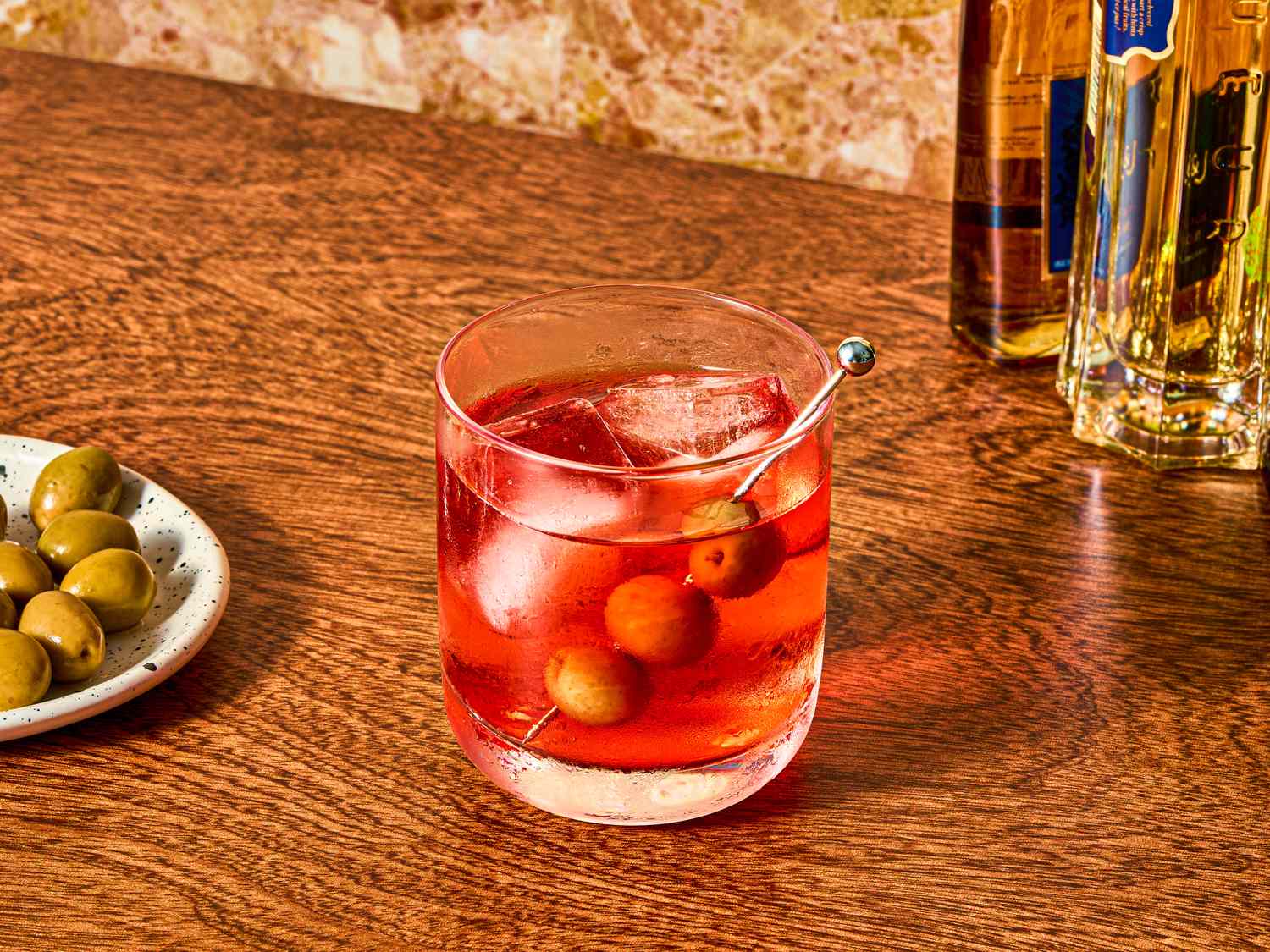 Glass of cocktail with ice and olives on side plate