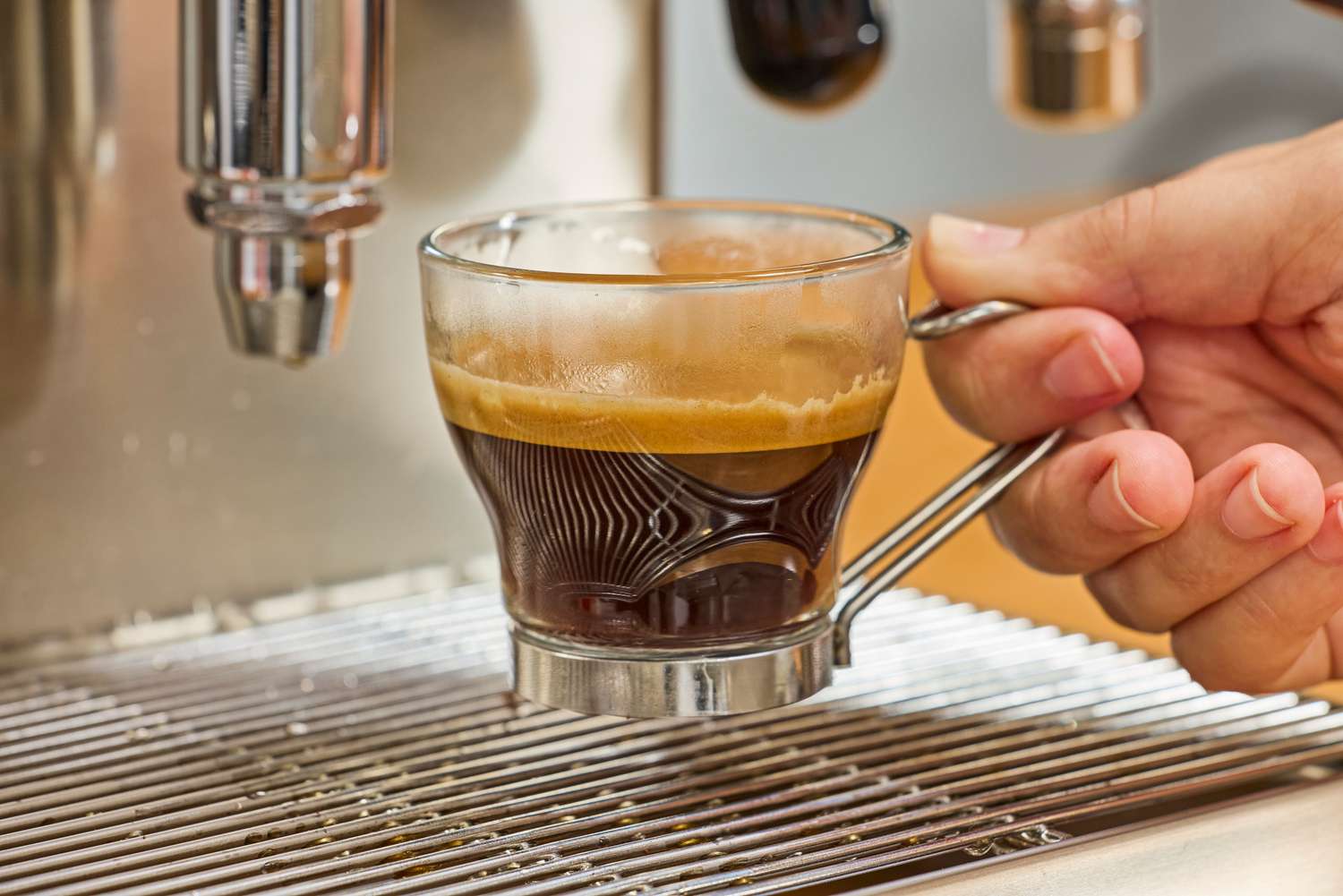 A close-up of a hand removing an espresso cup from the Lelit MaraX Espresso Machine PL62X-120