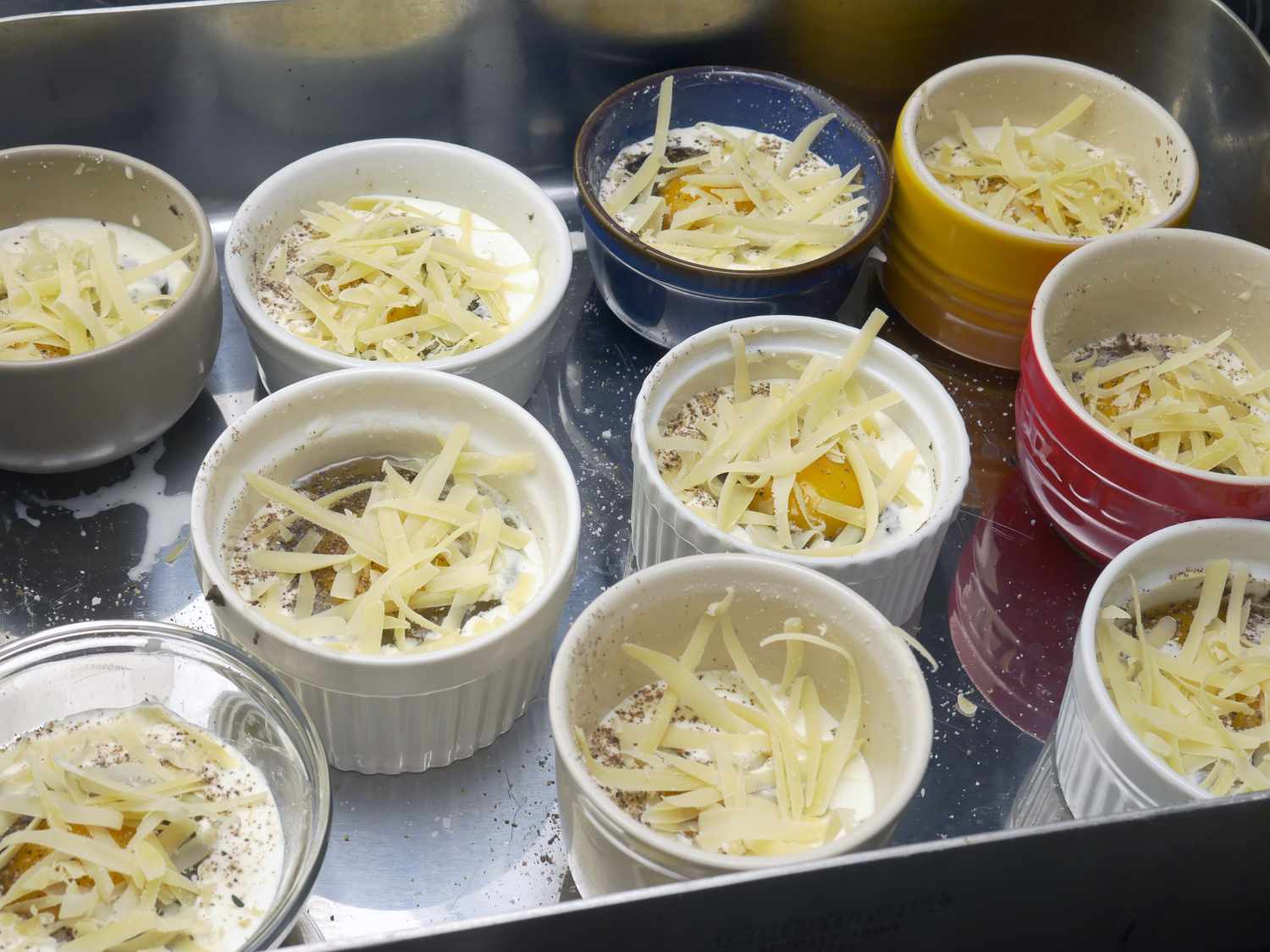 a bunch of ramekins with cheese an egg inside in a roasting pan