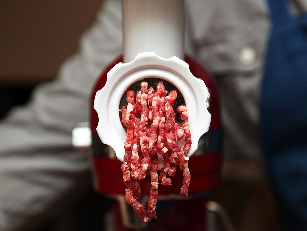 Ground meat emerging from the grinding attachment of a stand mixer.