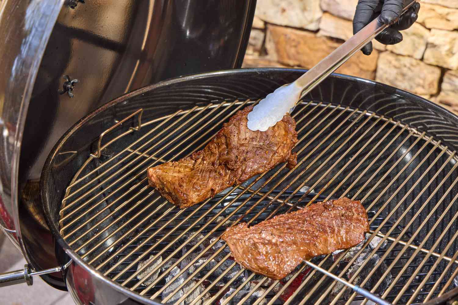A hand using tongs to move steak on the SNS Grills Slow 'N Sear Original 22-Inch Kettle Grill