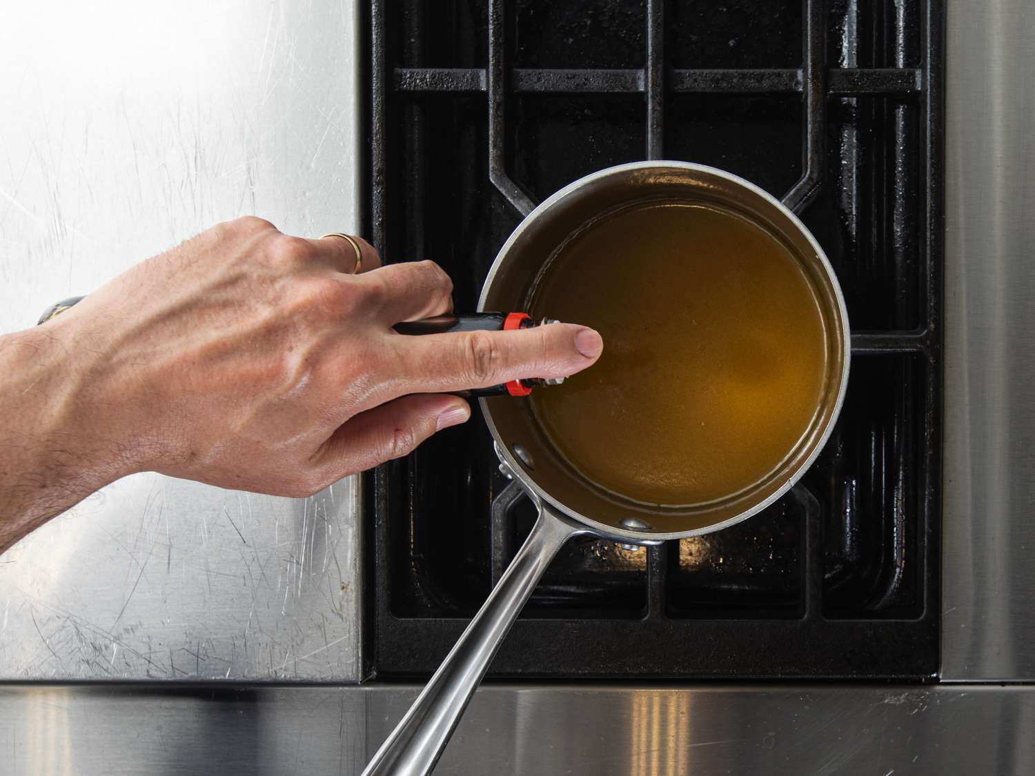 Adding soy sauce to simmered chicken jus in a small saucepan.