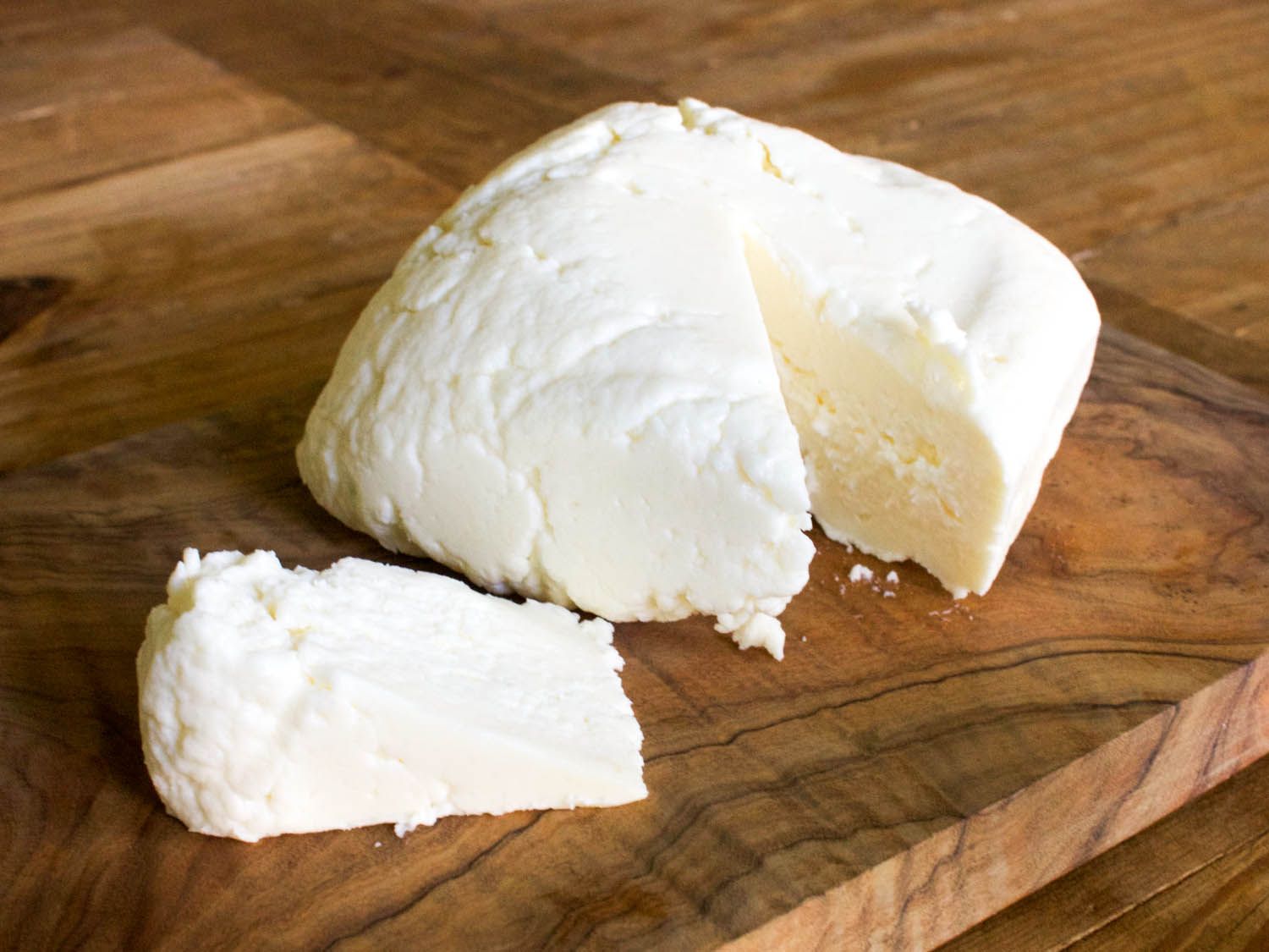 A cut of queso fresco resting on a cutting board.