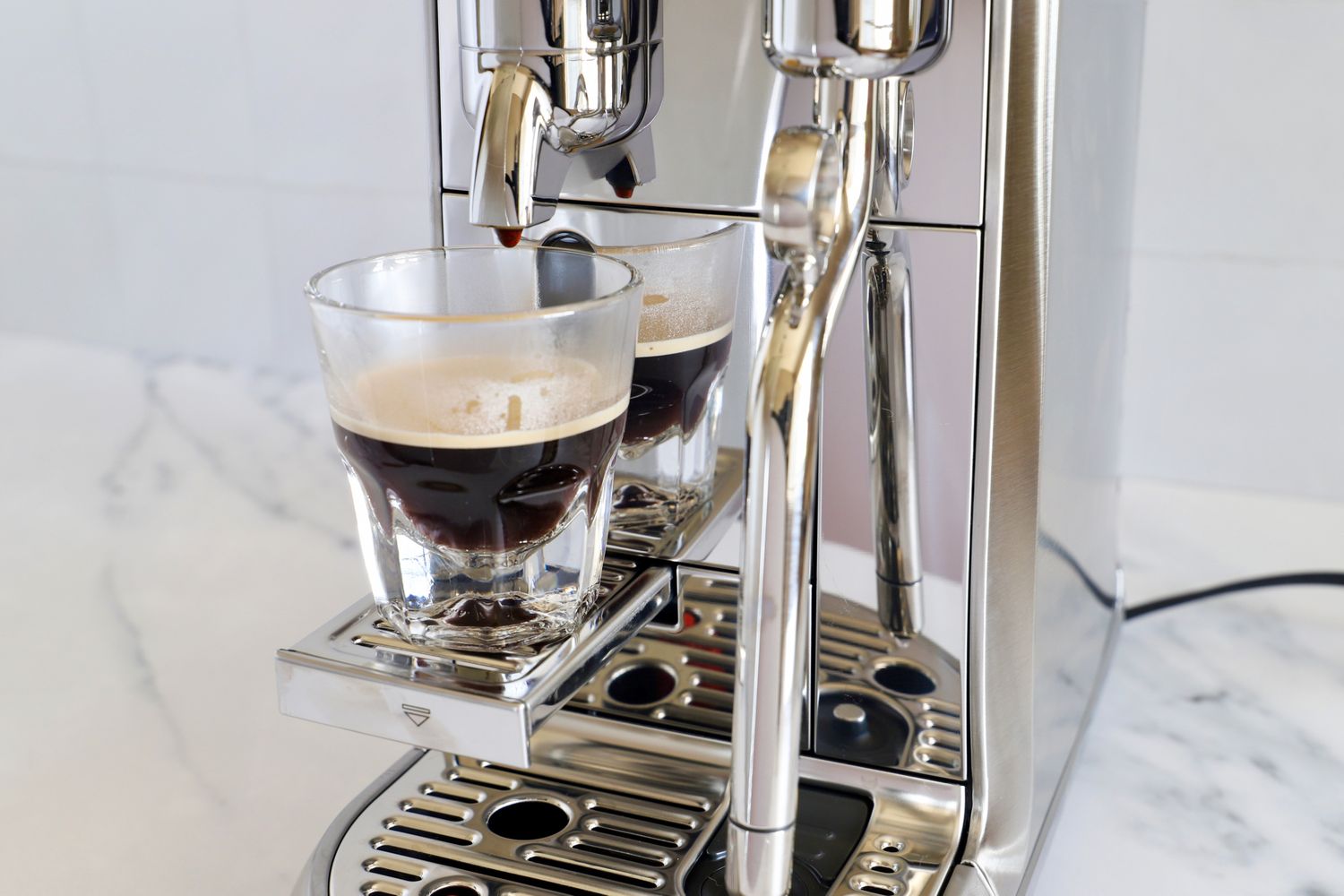 Espresso pouring from a coffee machine into a glass cup stainless steel design