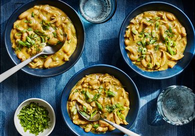 3 blue bowls of chicken, on a chambray textile with 2 glasses of sparking water 