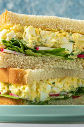 An egg salad sandwich, cut in half, with the two halves stacked on top of each other. The sandwich contains egg salad, butter lettuce, and thinly sliced radishes.
