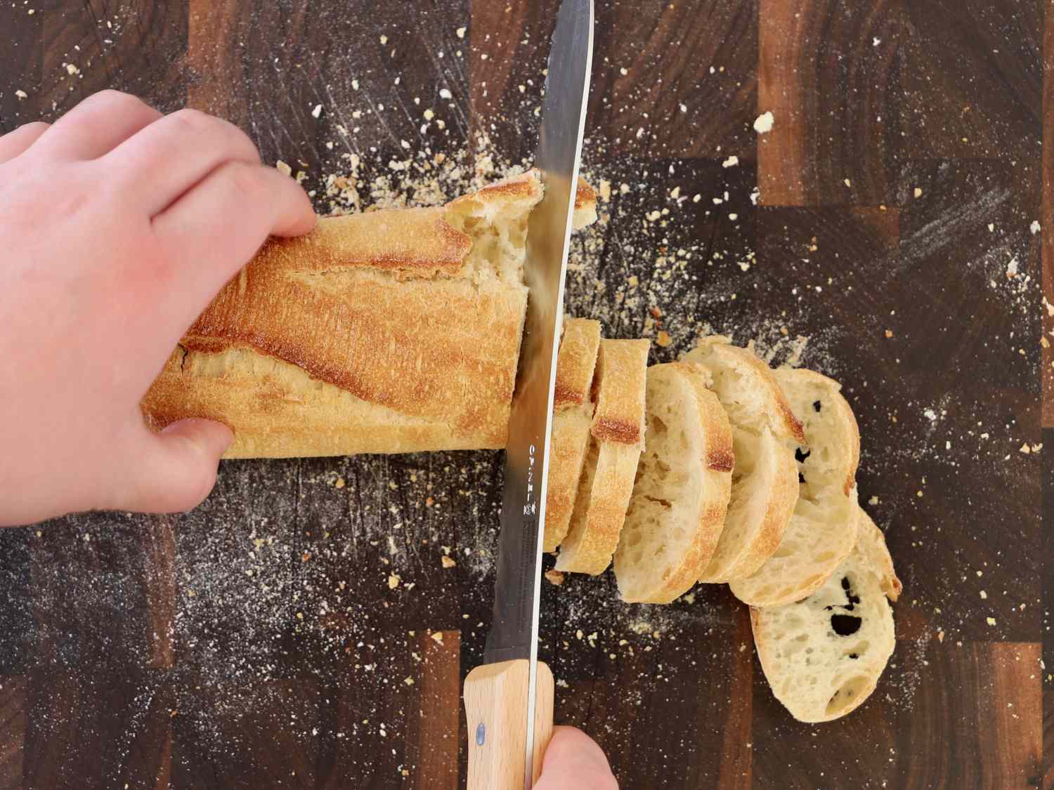 Hands slicing a baguette with the Opinel Parallele Serrated 8" Bread Knife
