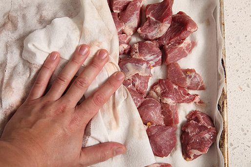 Patting chunks of raw pork dry with paper towels to remove surface moisture. 