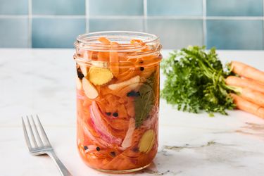 carrot ribbons in a jar with a fork on the side, with blue tile backsplash