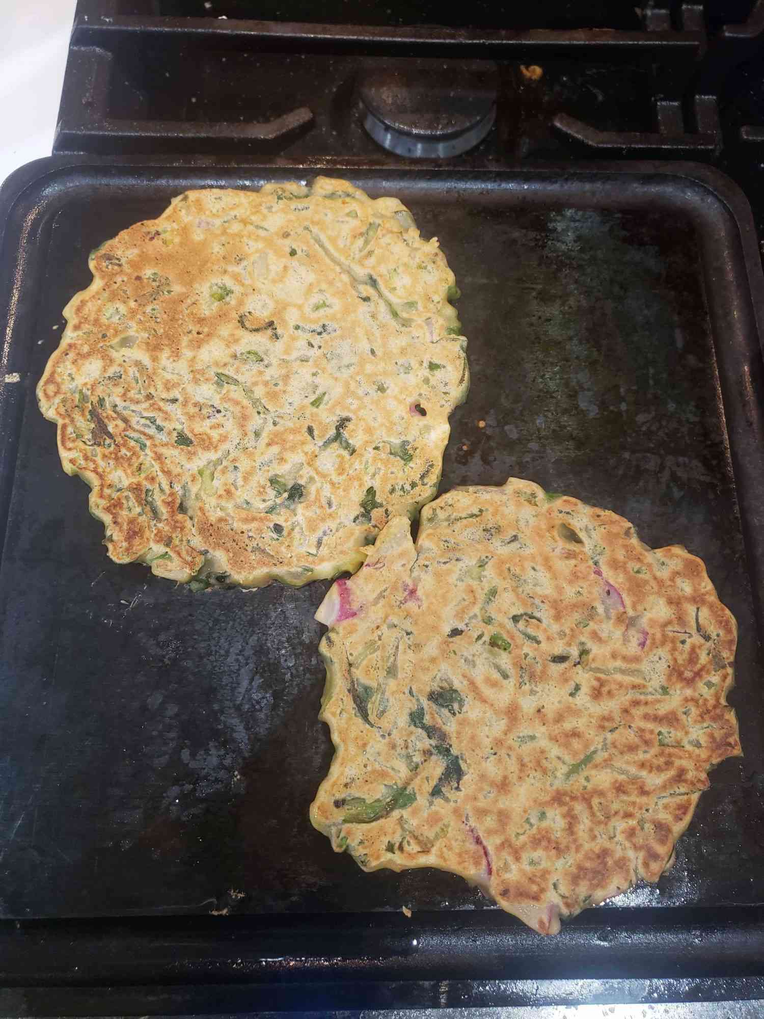 two savory pancakes cooking on a griddle