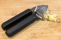 Garlic press with minced garlic on a wooden surface