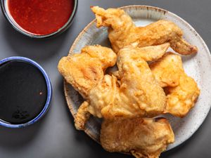 A small plate of Korean fried chicken wings with two dishes of sauce next to it.