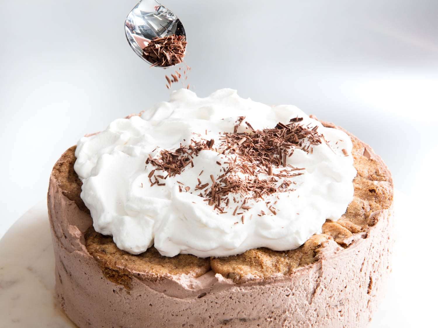 Spooning shaved chocolate over the whipped cream topping of an icebox cake.