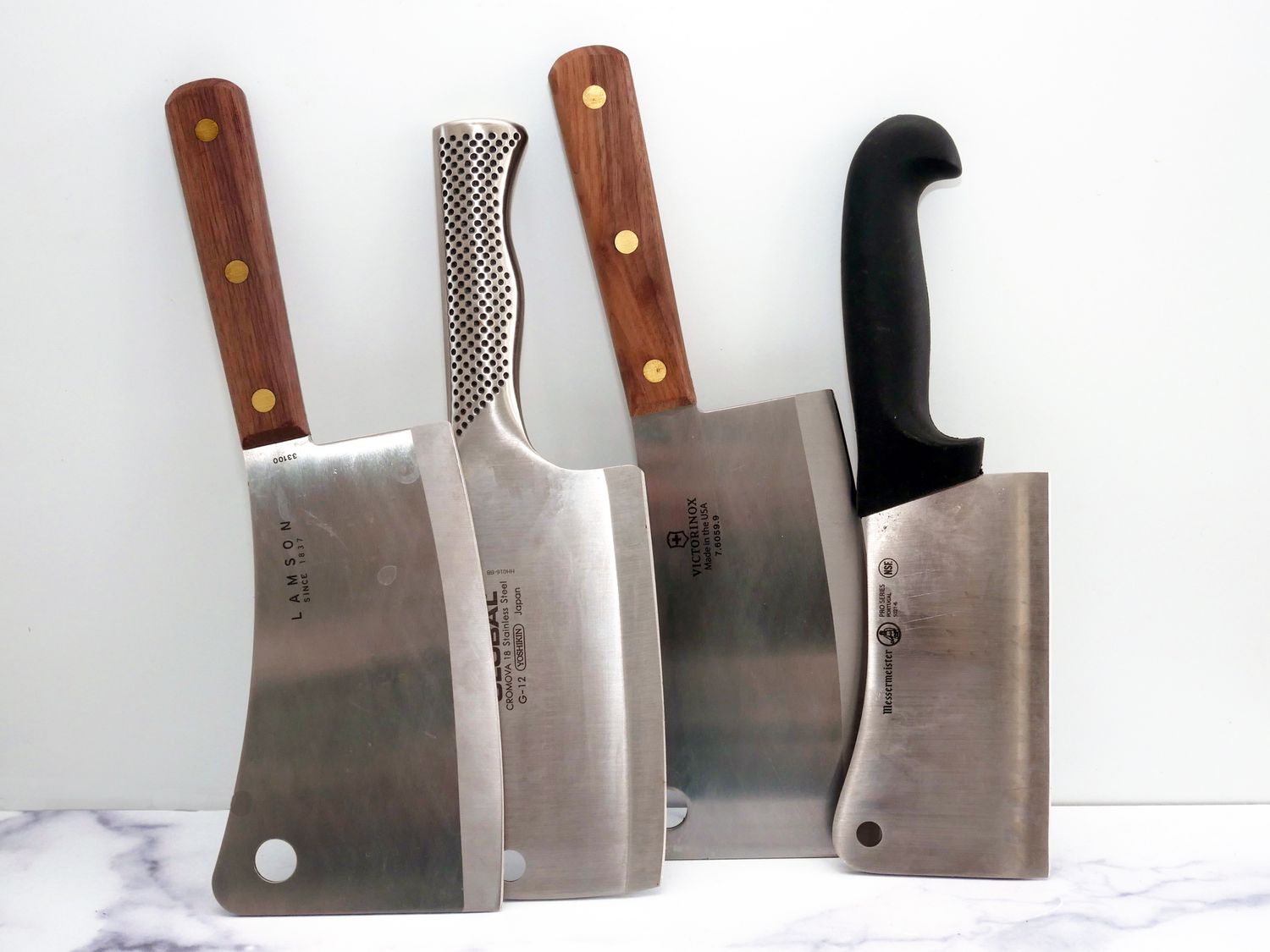 four meat cleavers standing on a marble surface with a white backdrop