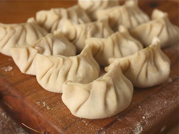 Pleated, uncooked dumplings lined up on a wooden cutting board.