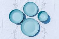 Four circular plates or bowls Year & Day The Outdoor Core Set of various sizes arranged on a decorative white cloth with a floral design