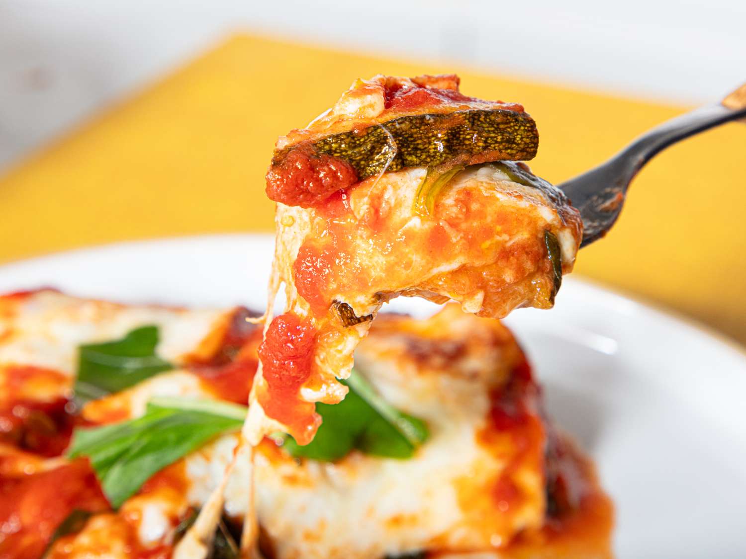 A fork holding a bite of zucchini parmesan topped with tomato sauce and melted cheese