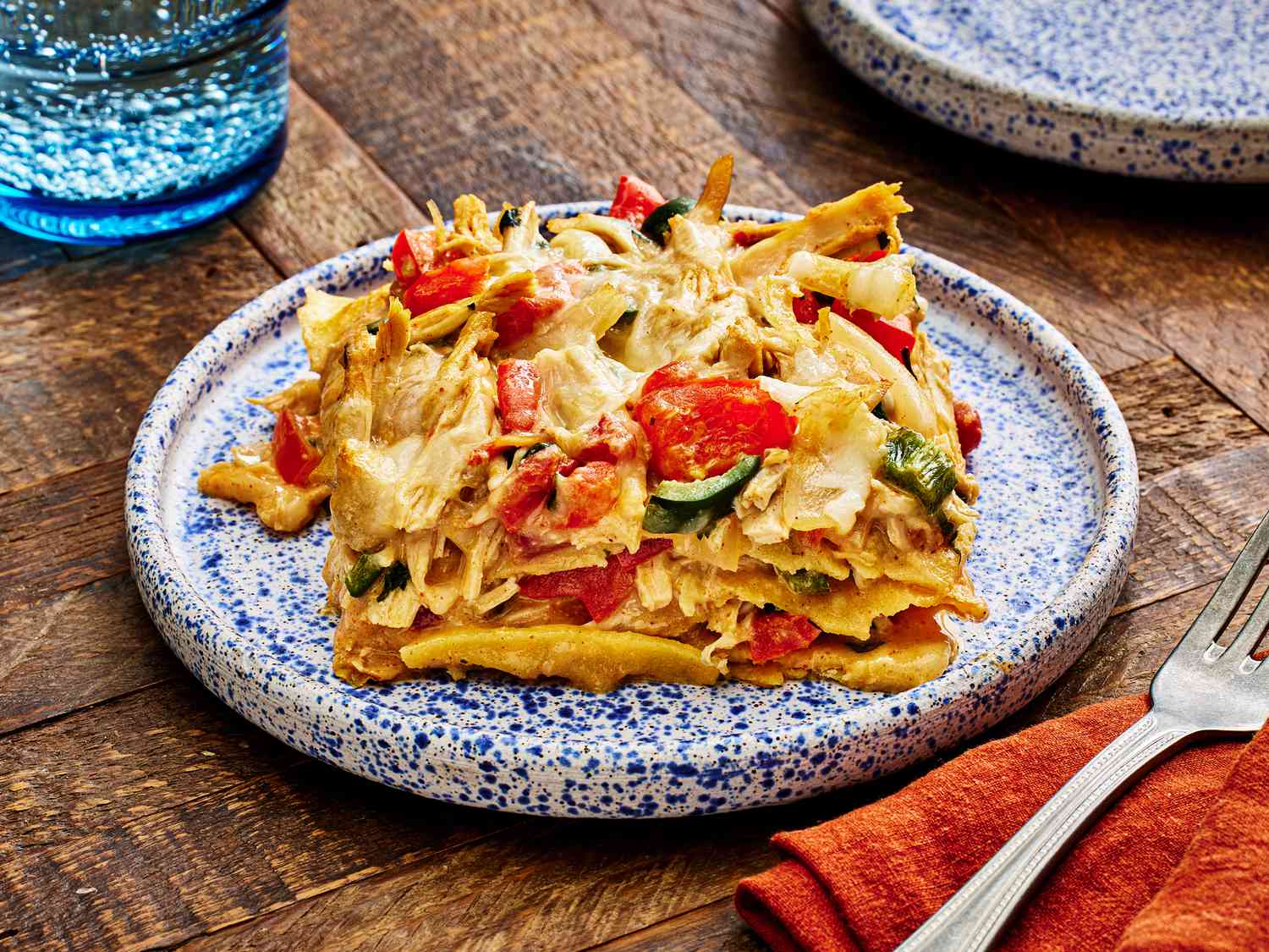 Large serving of King Casserole on a blue splatter plate. The dish is surrounded by a red napkin, a fork and a blue glass of sparkling water