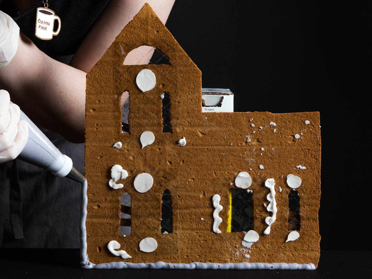 Piping lines and dollops of royal icing onto a wall of gingerbread to begin assembling the house