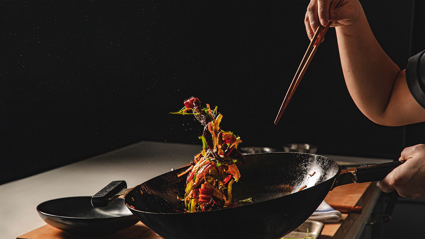 Colorful food suspended in air caused by a person tossing a while holding chopsticks in a dark kitchen.