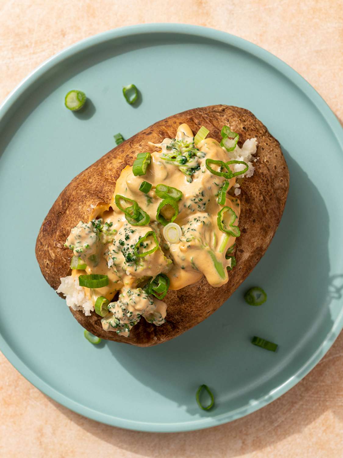 A vegan cheesy baked potato stuffed with broccoli cheese sauce on a blue plate,.