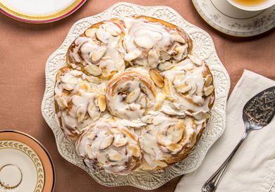 overhead of frangipane rolls on white platter, with 2 cups of tea on a pink tablecloth 