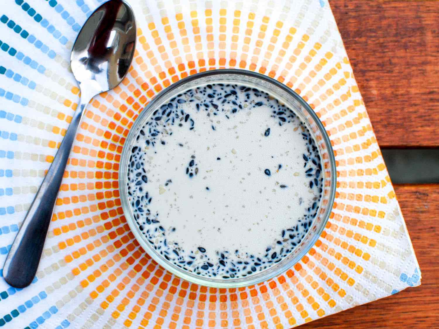 Overhead view of black sesame and honey pudding, served in a small bowl on a colorful sunburst-patterned cloth.