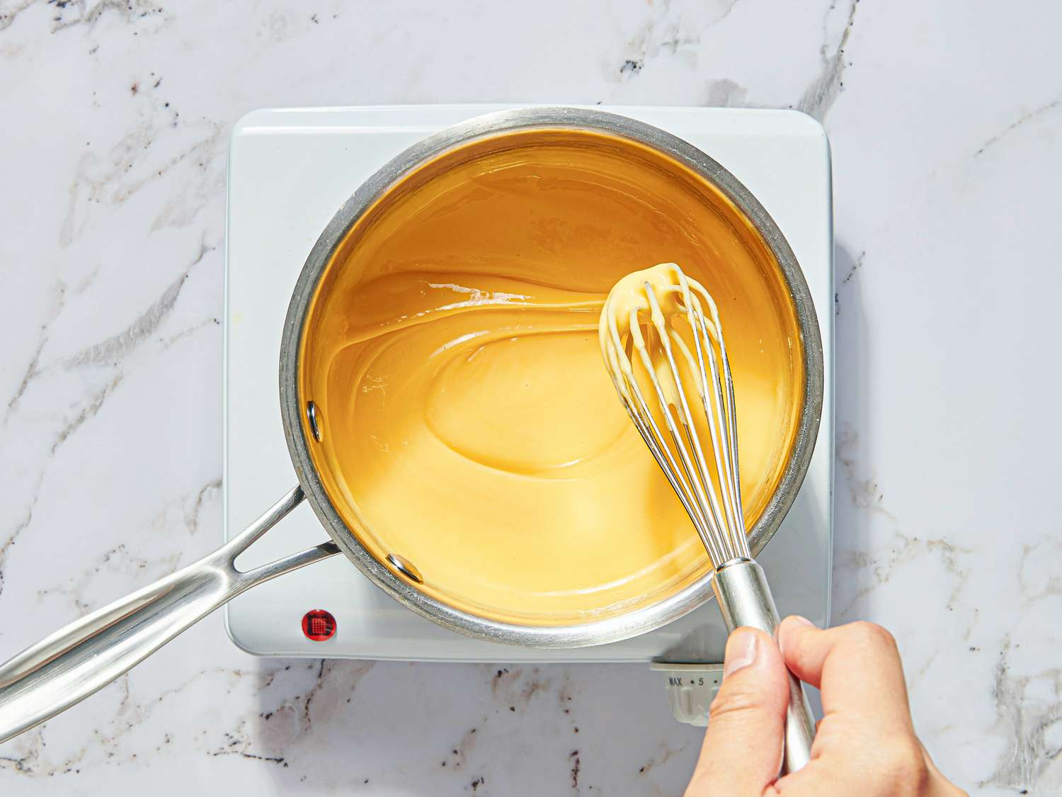 Overhead view of whisk lifting cheese sauce