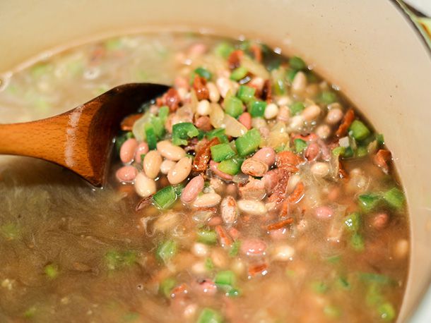 Stirring a pot of beans with bacon and chopped peppers.