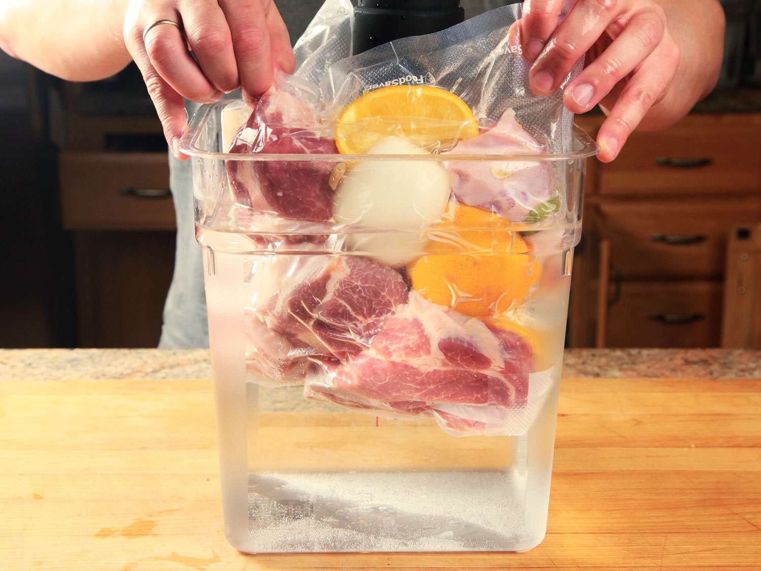 Placing vacuum-sealed bag of pork shoulder and aromatics in a water bath to cook sous vide for carnitas.