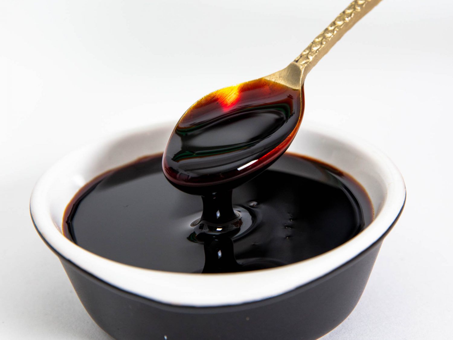 A small spoon lifting a spoonful of kecap manis (Indonesian sweet soy sauce) from a bowl