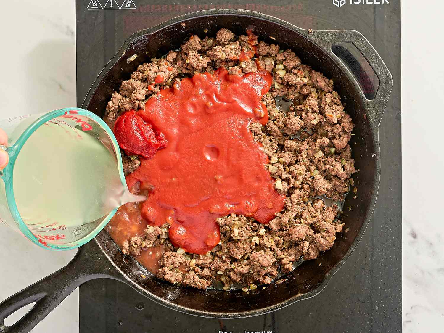Ground meat cooking in a skillet with tomato sauce being added