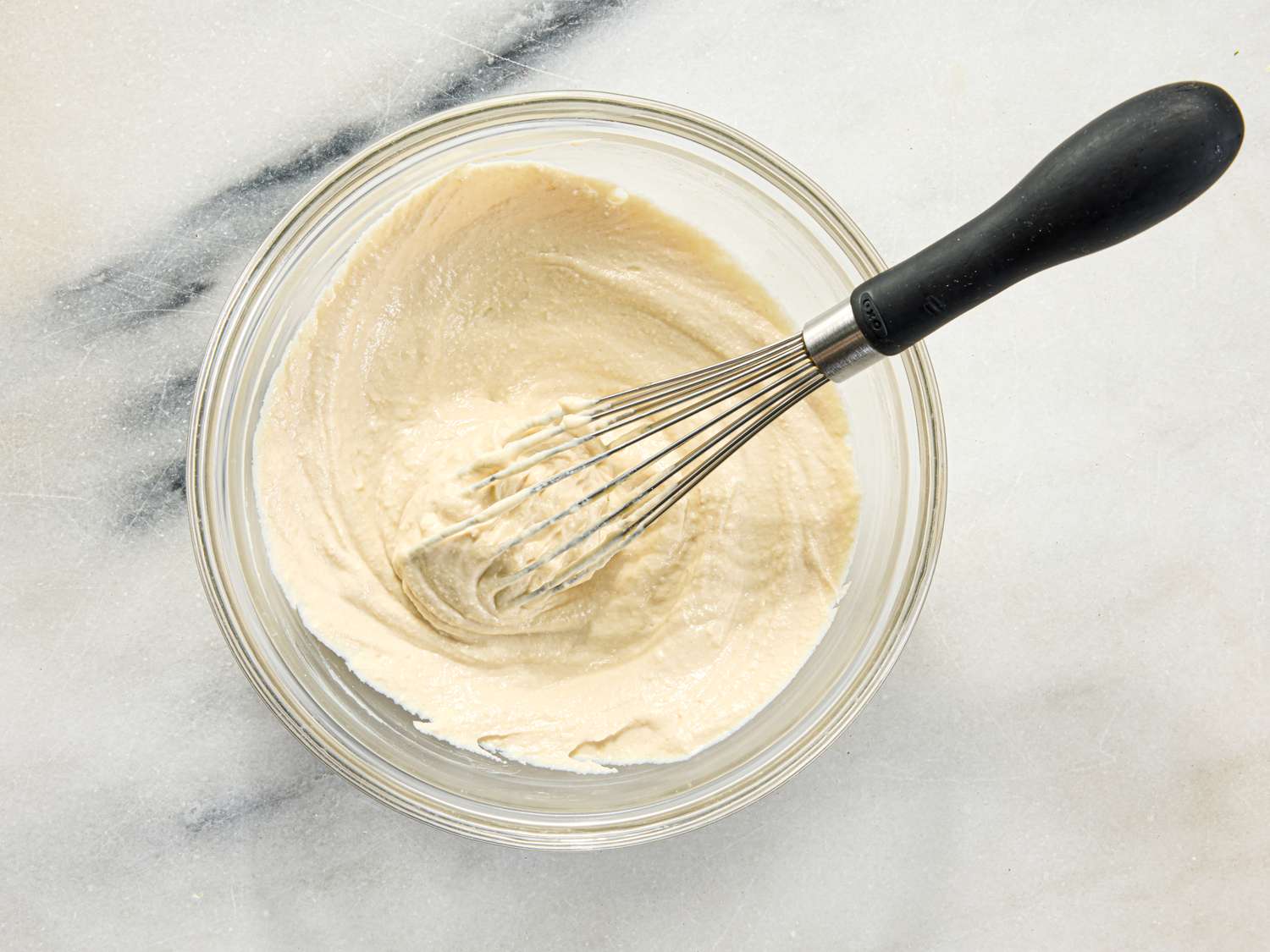 Whisk in a glass bowl mixing batter or sauce on a marble surface