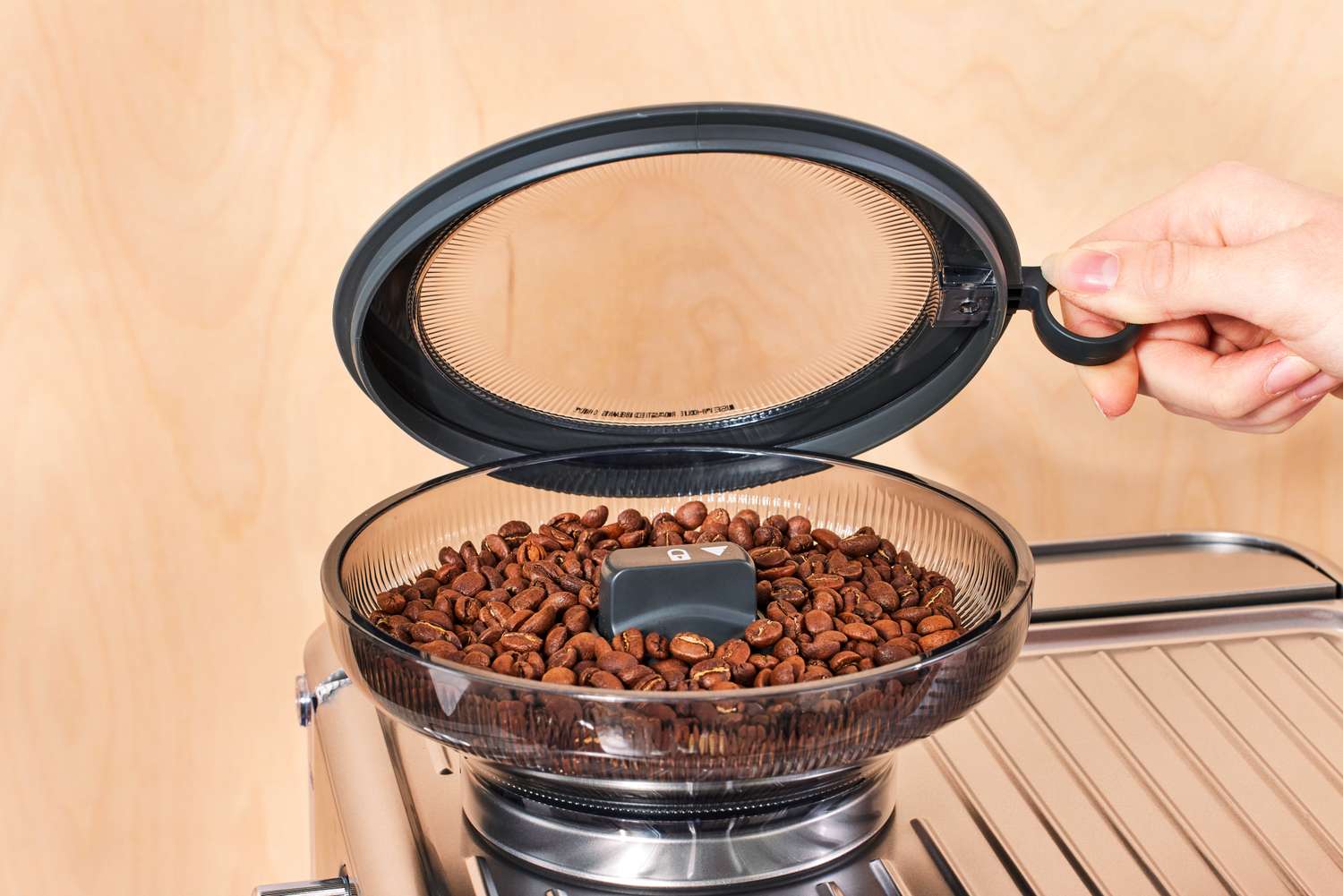 A person lifting up the lid of the coffee grinder section of the Breville Barista Touch Impress Espresso Machine with Grinder