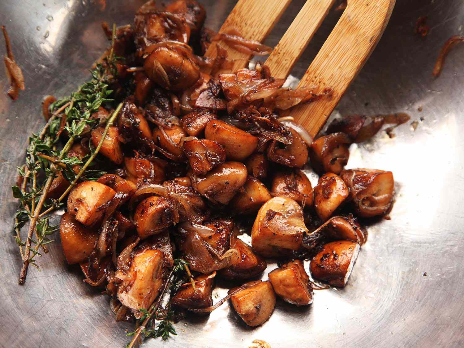 Cooked mushrooms and herbs in a bowl being stirred with a wooden spatula. 