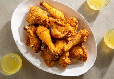 Platter of batter-fried chicken pieces flanked by yellow drinks on marble surface