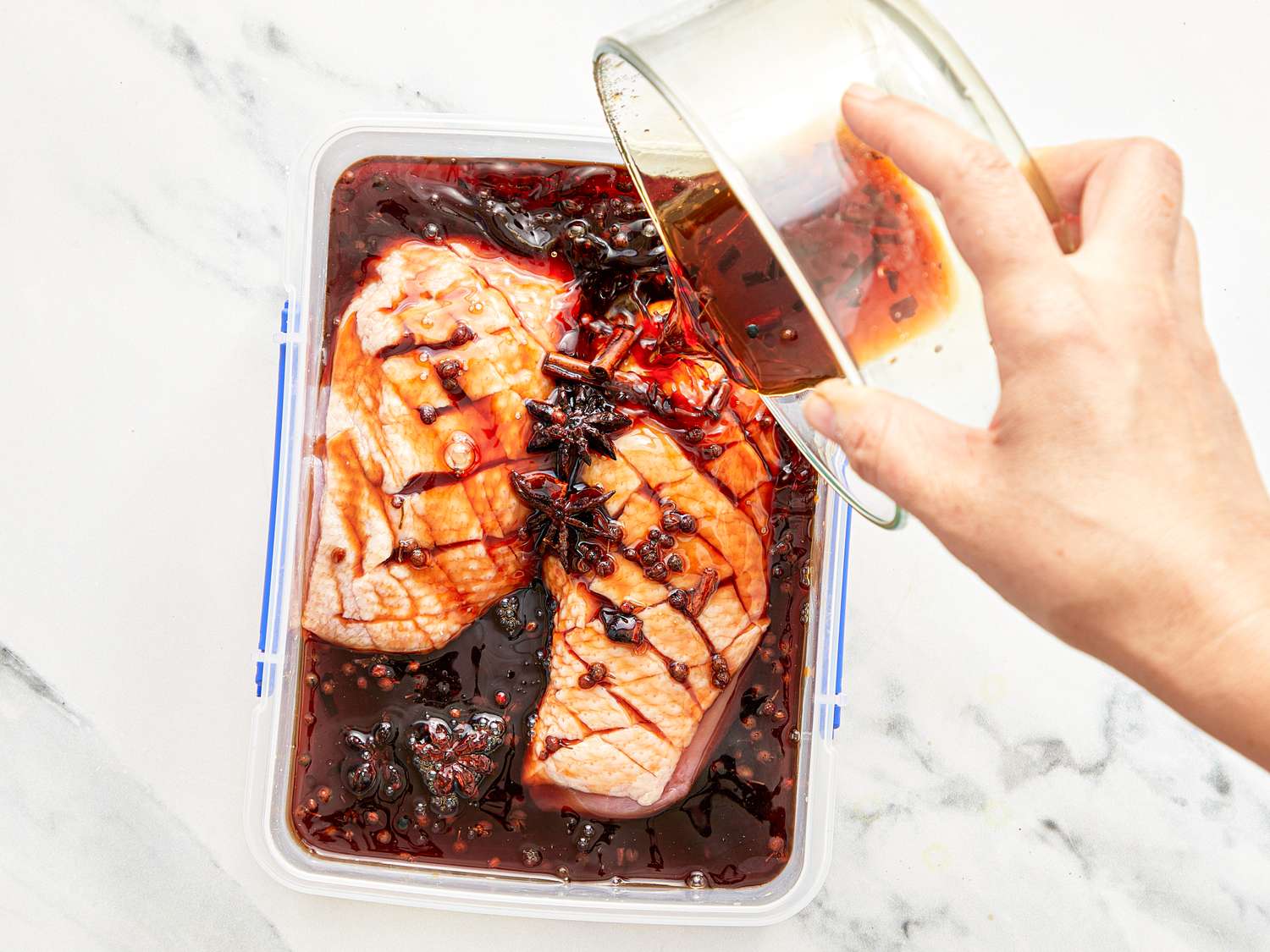 Duck breasts being marinated in a rectangular container with liquid being poured over them