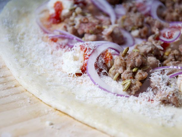 The par-cooked and crumbled sausage is added to a round of pizza dough, along with sauce, cheese, and thinly sliced red onion.