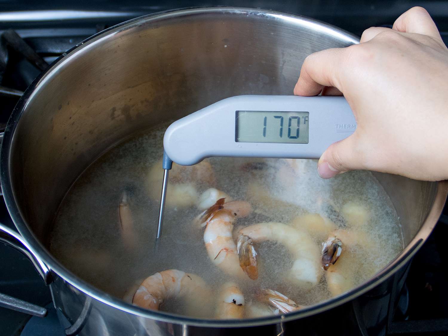 A thermometer displaying a temperature of 170 degrees F in the pot of cooked shrimp.