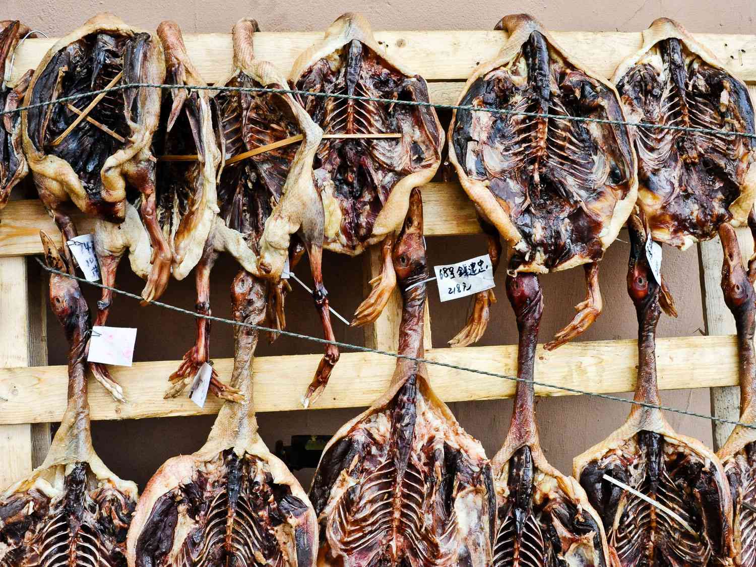 Cured and dried duck hang from a wooden display rack.