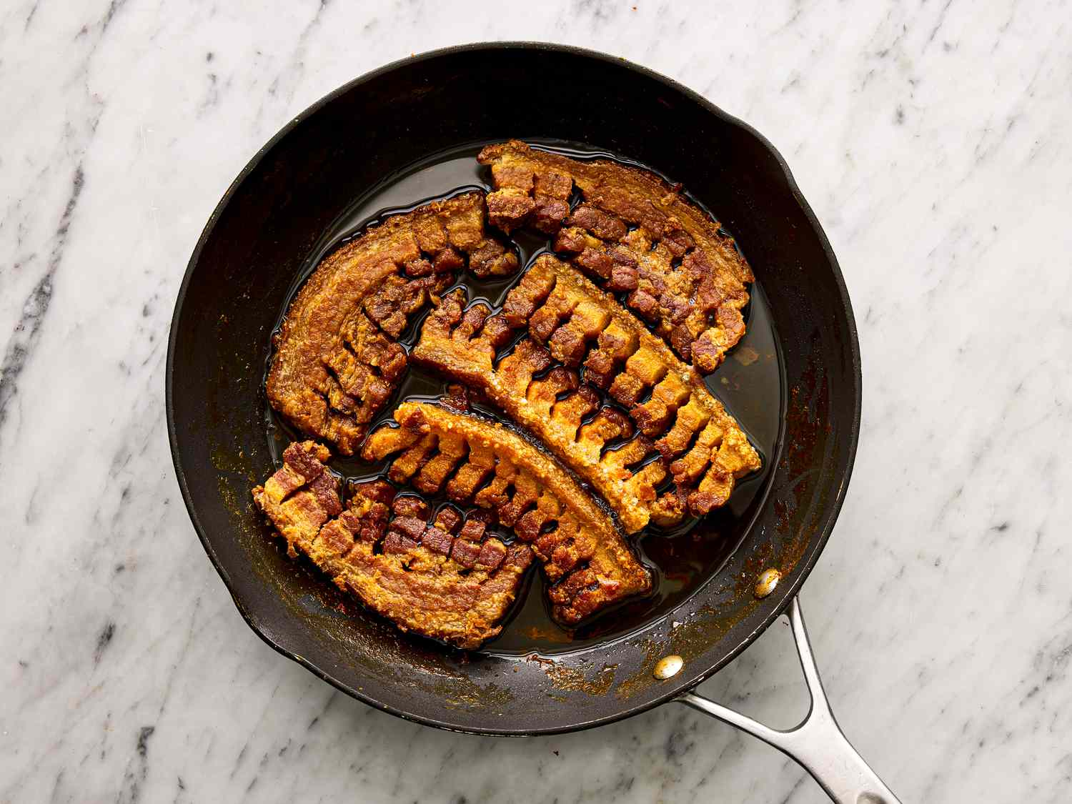 Overhead view of pork belly cooked in pan and resting in its juices.